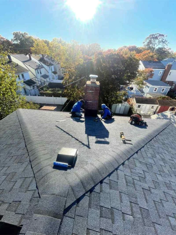Roofer installing new step flashing where a shingle roof meets a chimney
